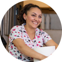 smiling woman with dark hair and a blouse with a multi-colored hearts pattern