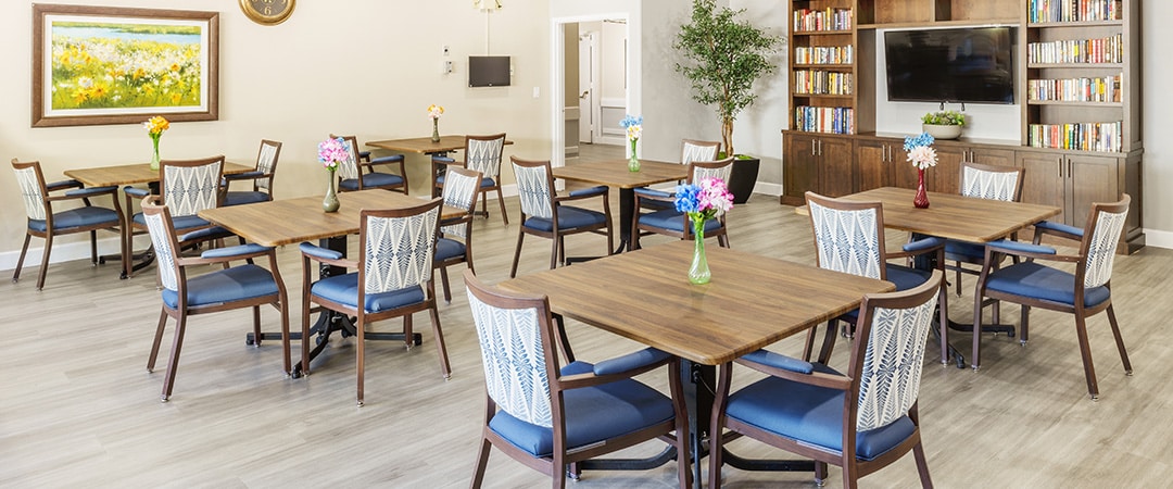 Dining room with flower arrangements on tables and bookcase with a TV centered