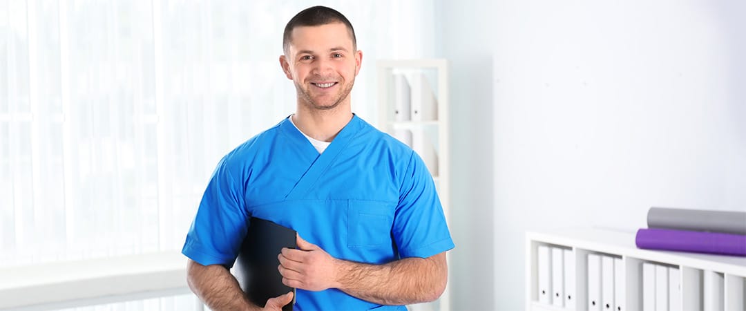 Male nurse wearing blue scrubs and carrying a patient chart
